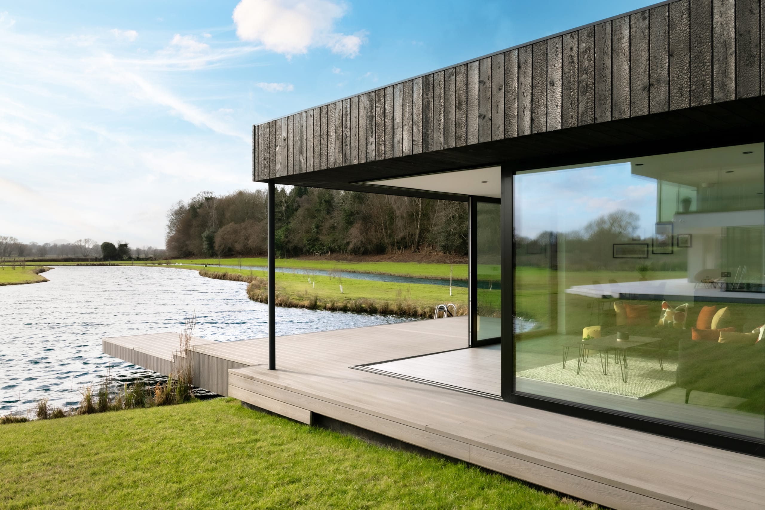 Modern lakeside home with charred timber cladding, floor-to-ceiling windows, and wooden deck overlooking serene water